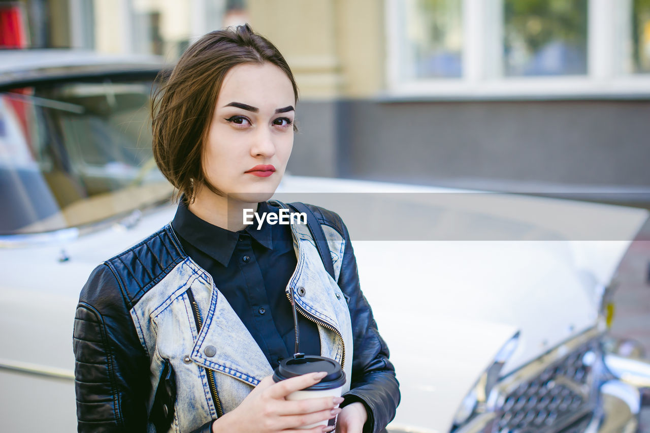 Portrait of confident young woman with disposable cup standing in city