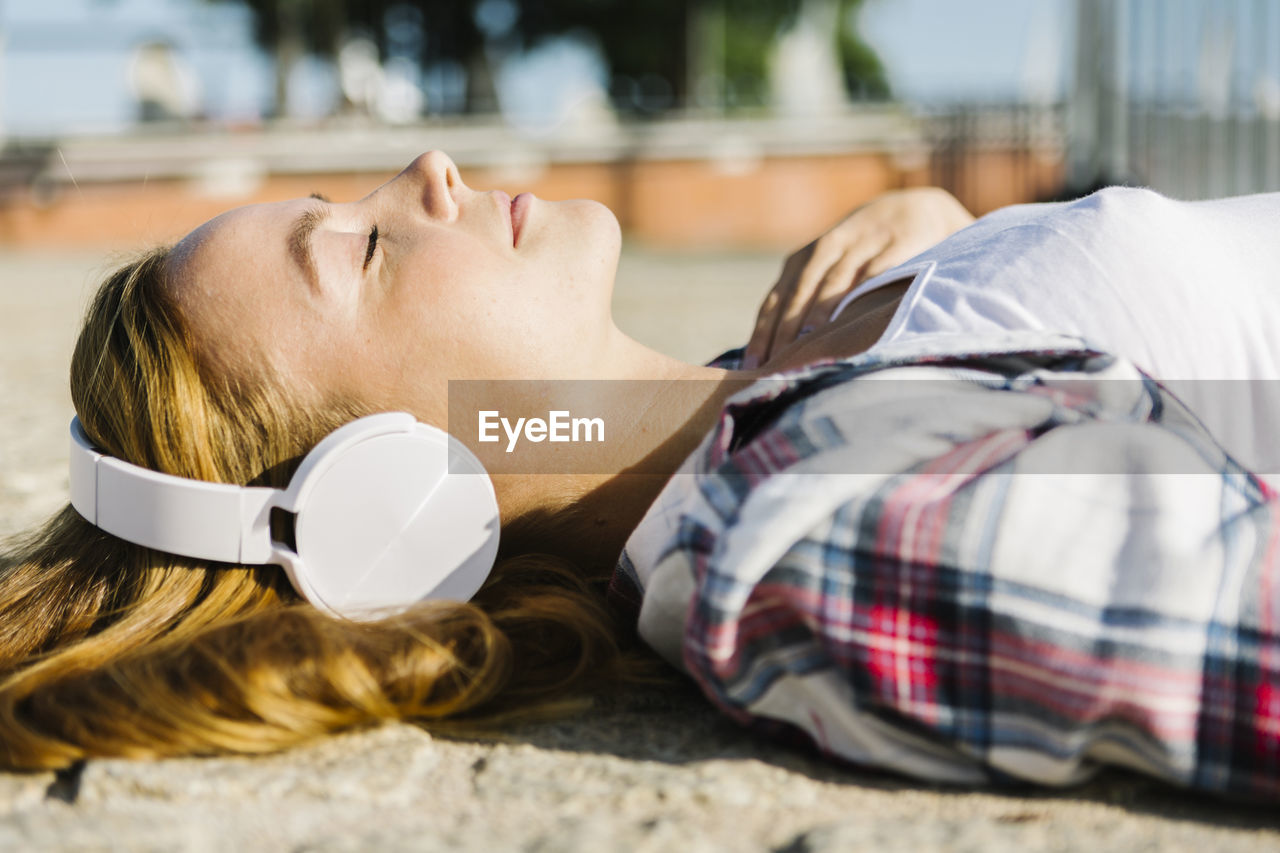 Woman lying on back listening music through headphone during sunny day