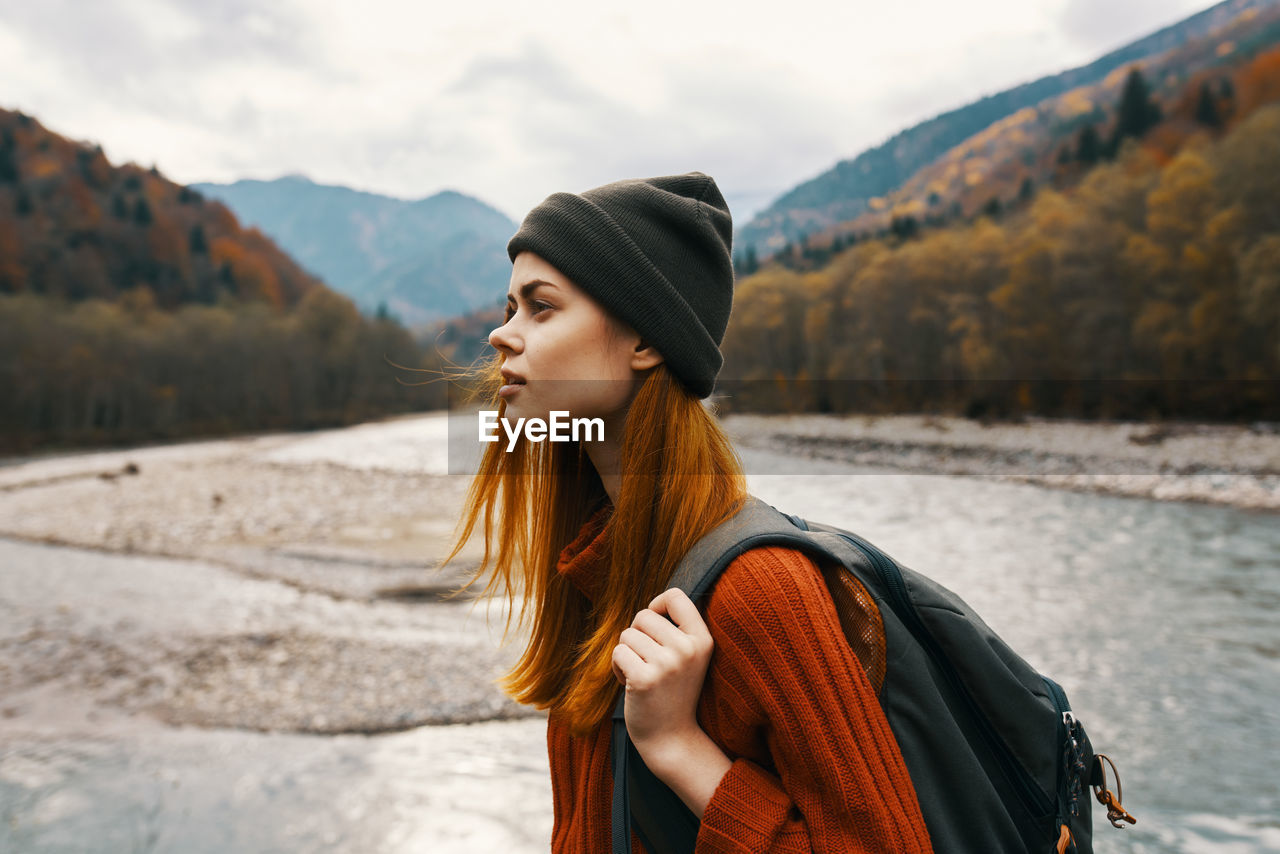 YOUNG WOMAN LOOKING AWAY WHILE STANDING ON MOUNTAINS