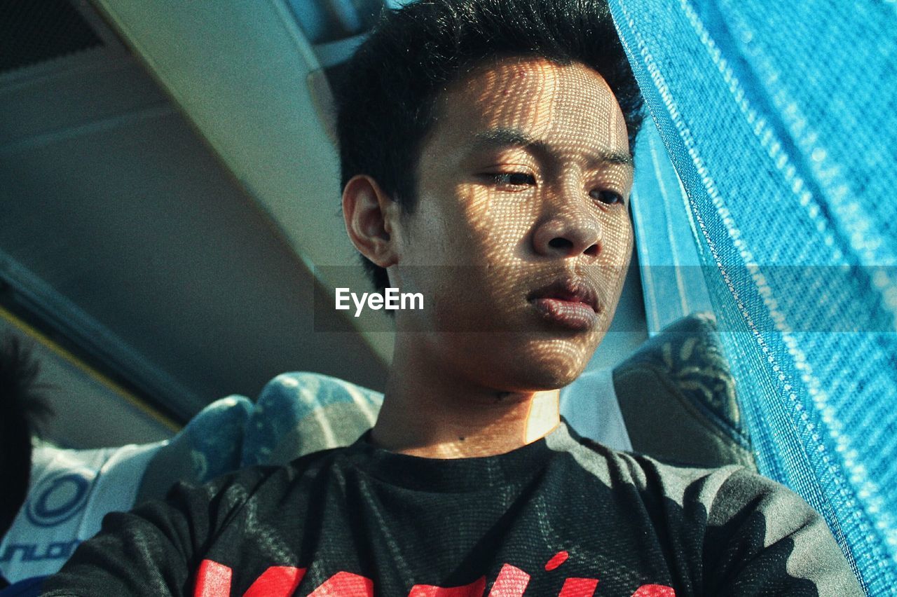 Low angle view of young man sitting in bus on sunny day