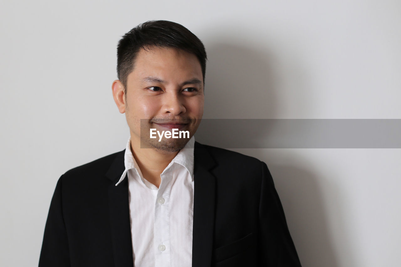 Close-up of man smiling while wearing blazer by white wall