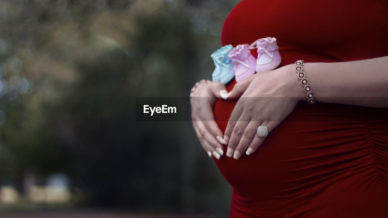 Midsection of pregnant woman with baby booties and hands on stomach standing outdoors