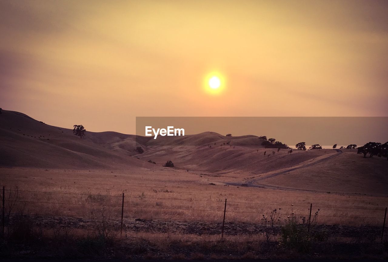 SCENIC VIEW OF FIELD AGAINST BRIGHT SUN DURING SUNSET