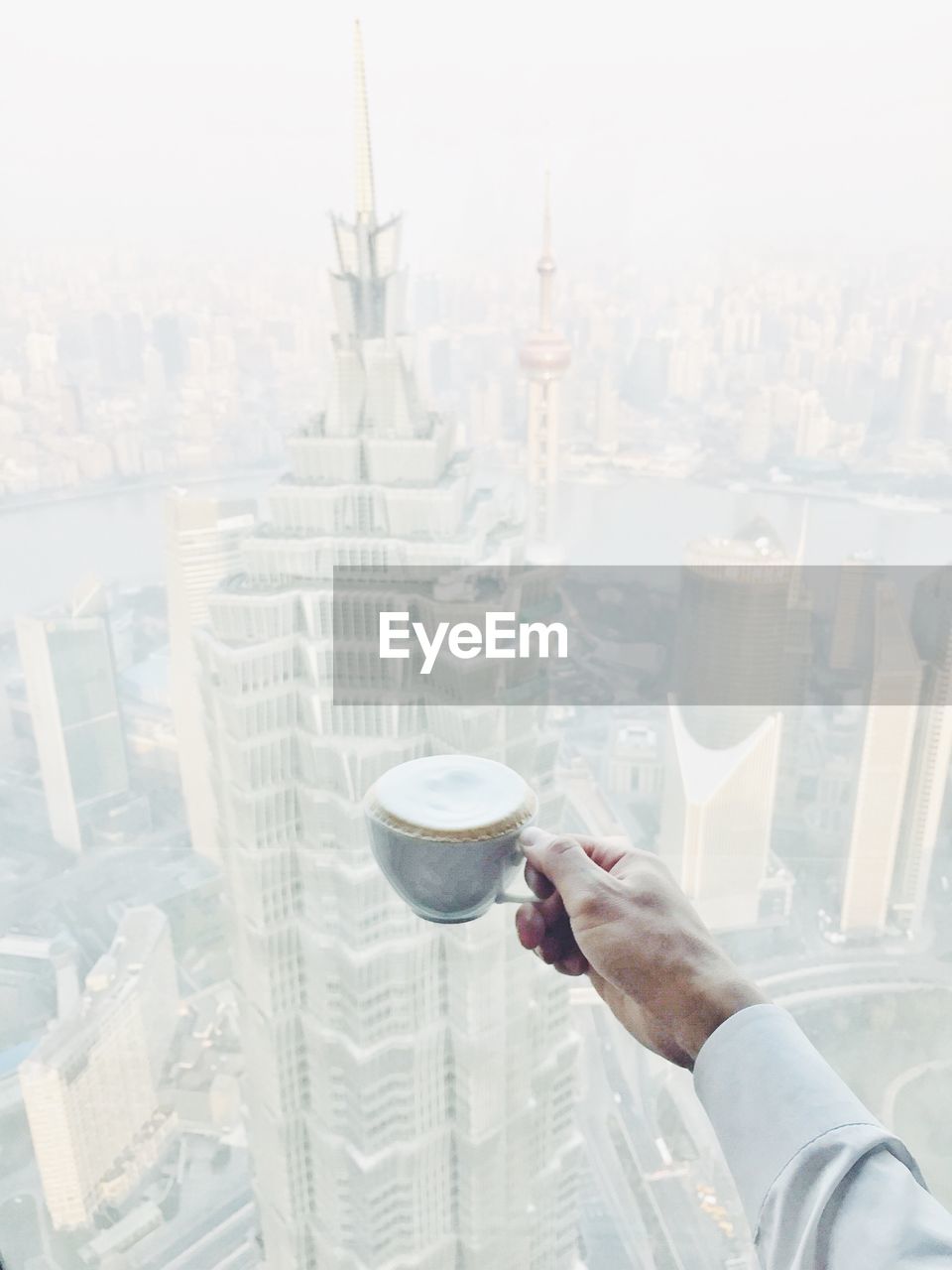 High angle view of hand holding coffee cup against skyscrapers in city