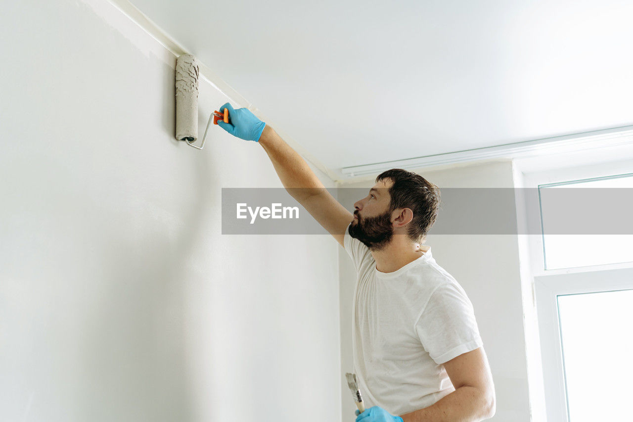 Caucasian bearded man painting wall with paint roller. painting apartment, renovating home