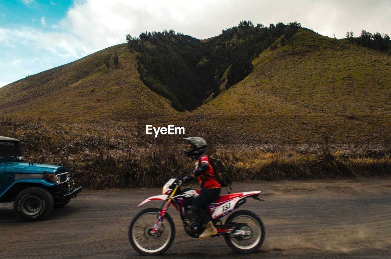 MAN RIDING MOTORCYCLE ON ROAD AGAINST MOUNTAIN RANGE