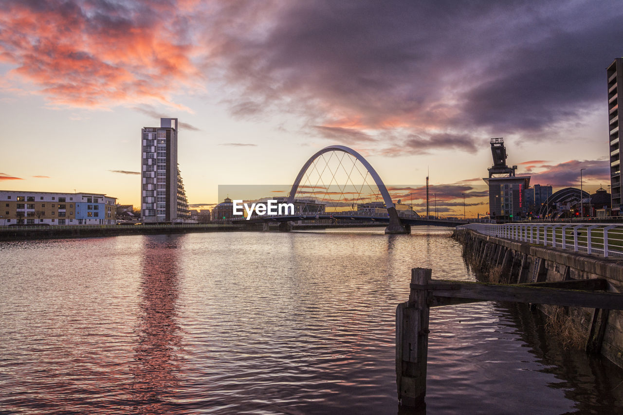 Bridge over clyde river against cloudy sky in city during sunset