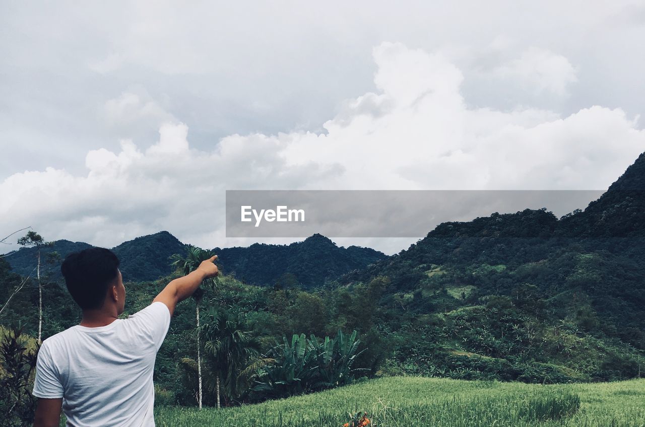 Rear view of man pointing at mountain against sky