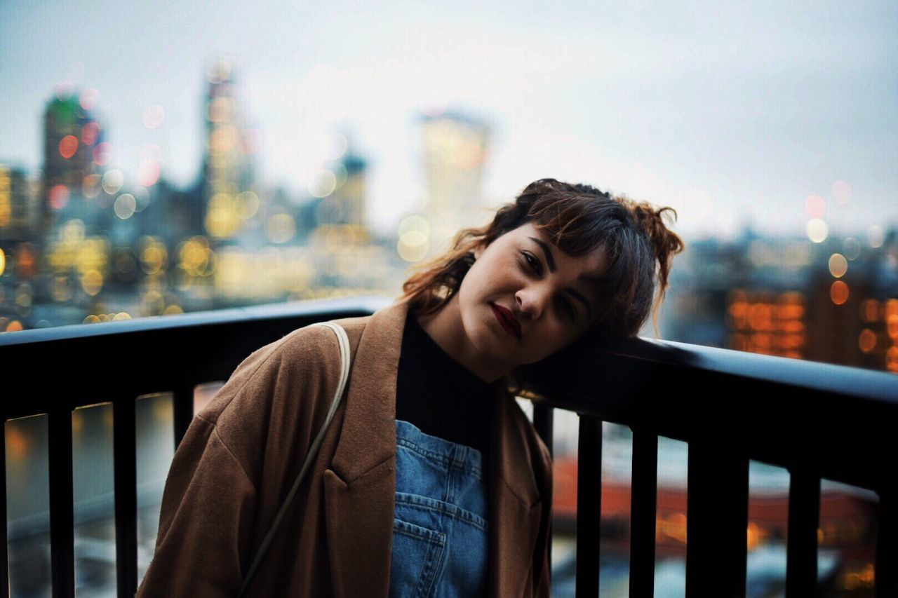 PORTRAIT OF YOUNG MAN LEANING ON RAILING IN CITY