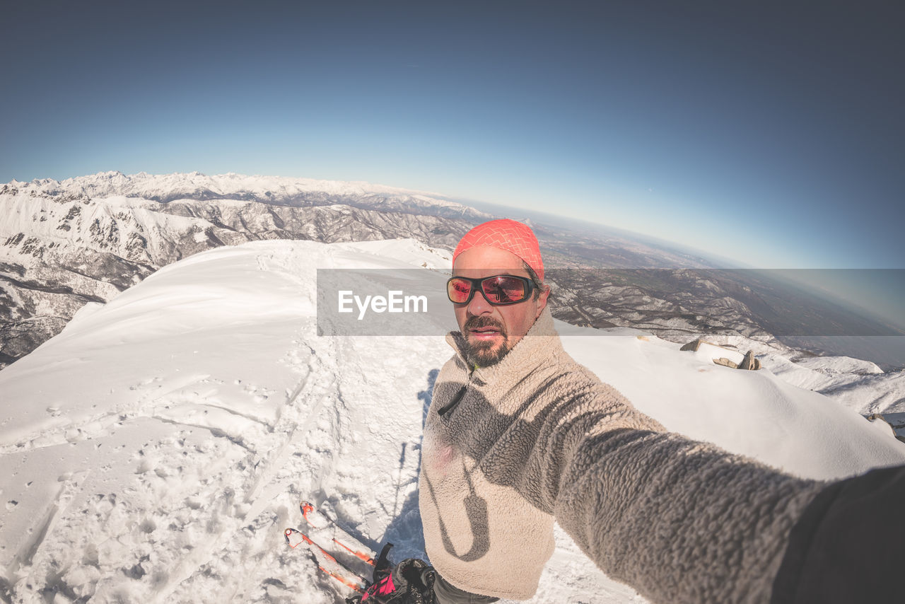 Portrait of man taking selfie while standing on snowy field