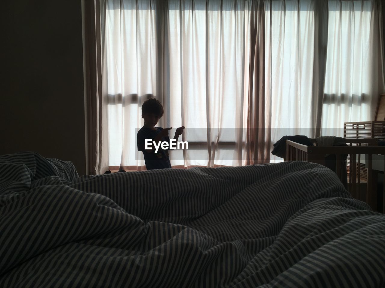 Boy gesturing while standing by bed at home