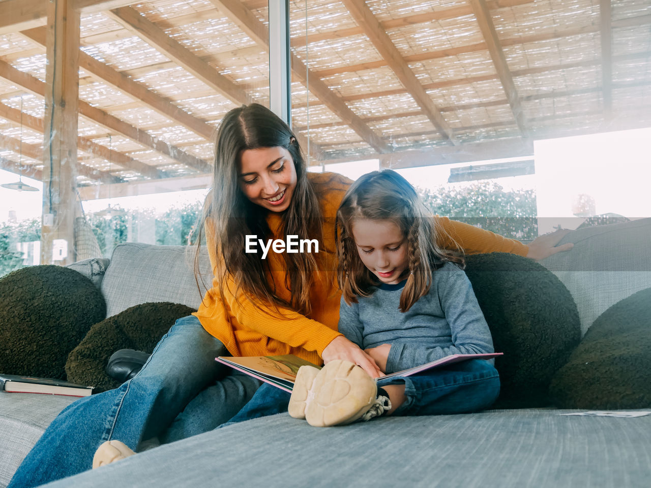 Content female teen pointing with finger at textbook page while spending time with sibling on couch at home