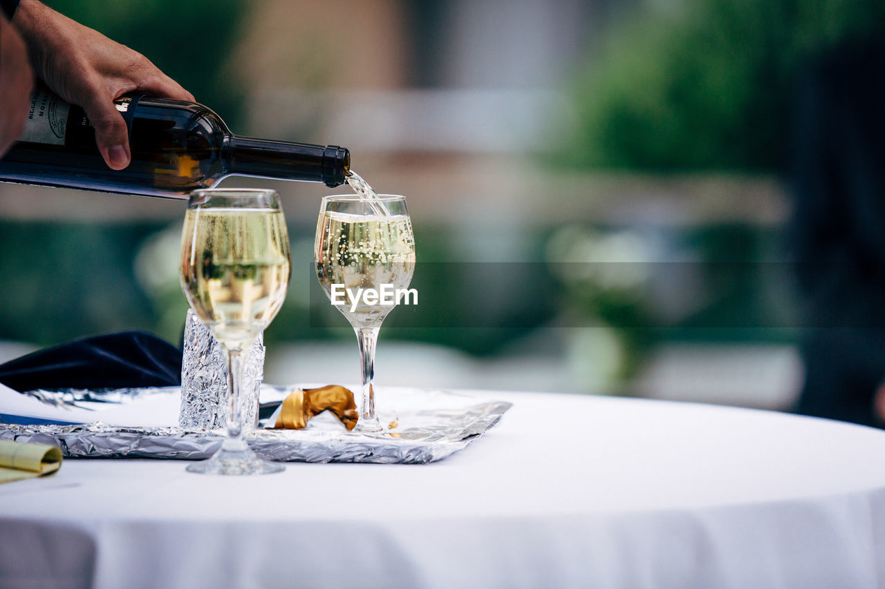 Cropped hand of person pouring drink in glass on table