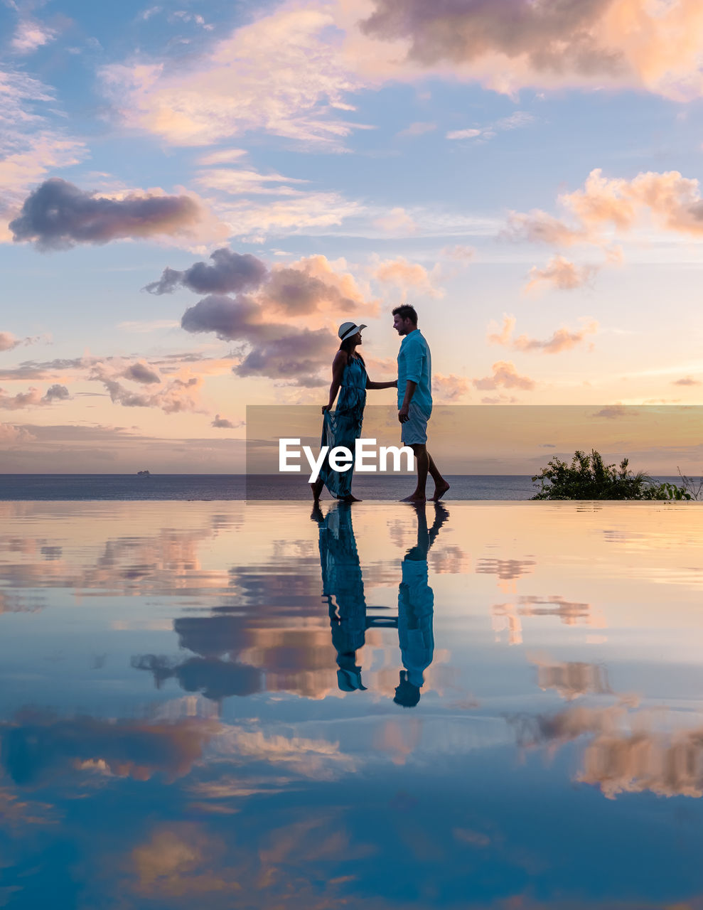 rear view of woman standing on shore at beach against sky during sunset