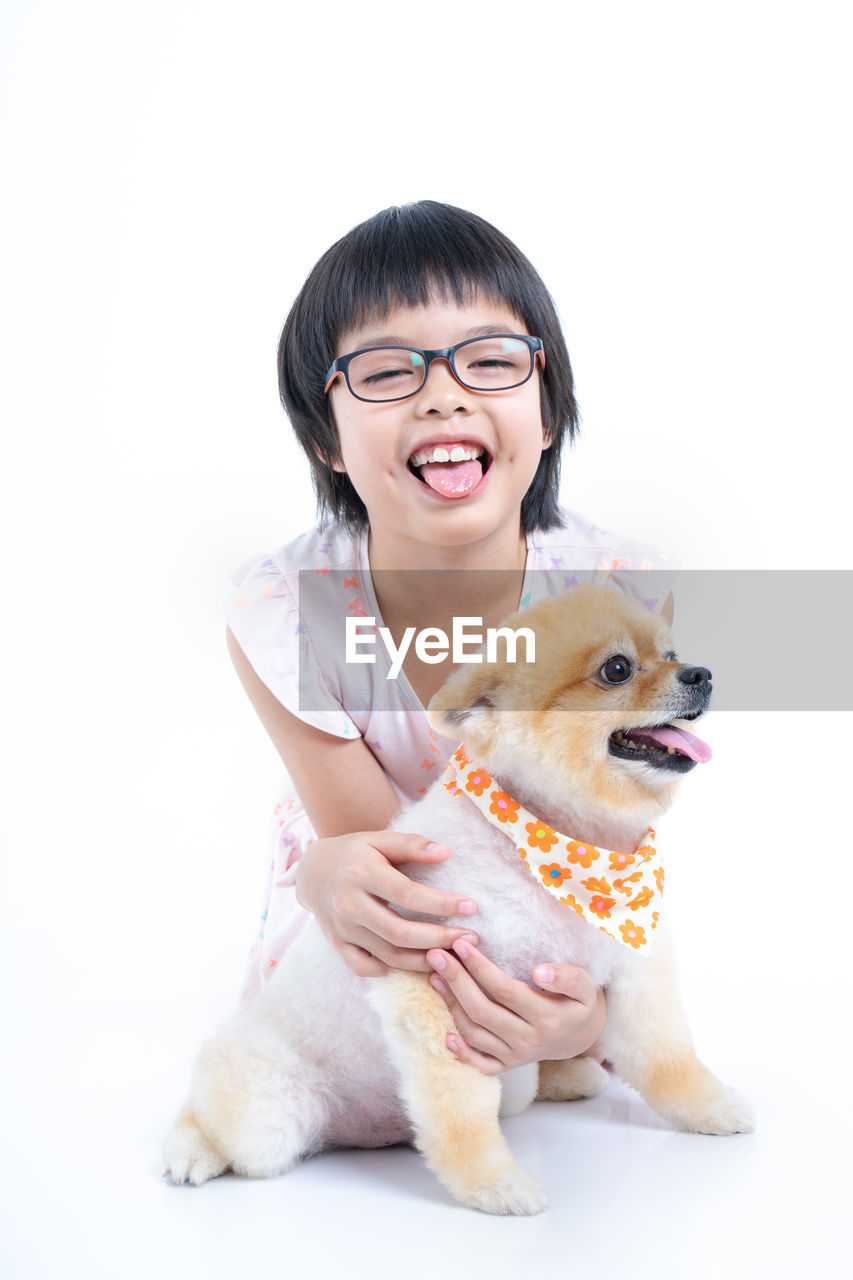 Portrait of smiling girl with dog sitting against white background