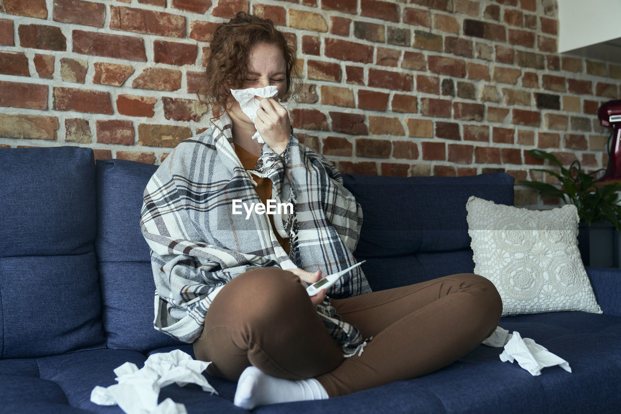 portrait of young man using mobile phone while sitting on sofa at home