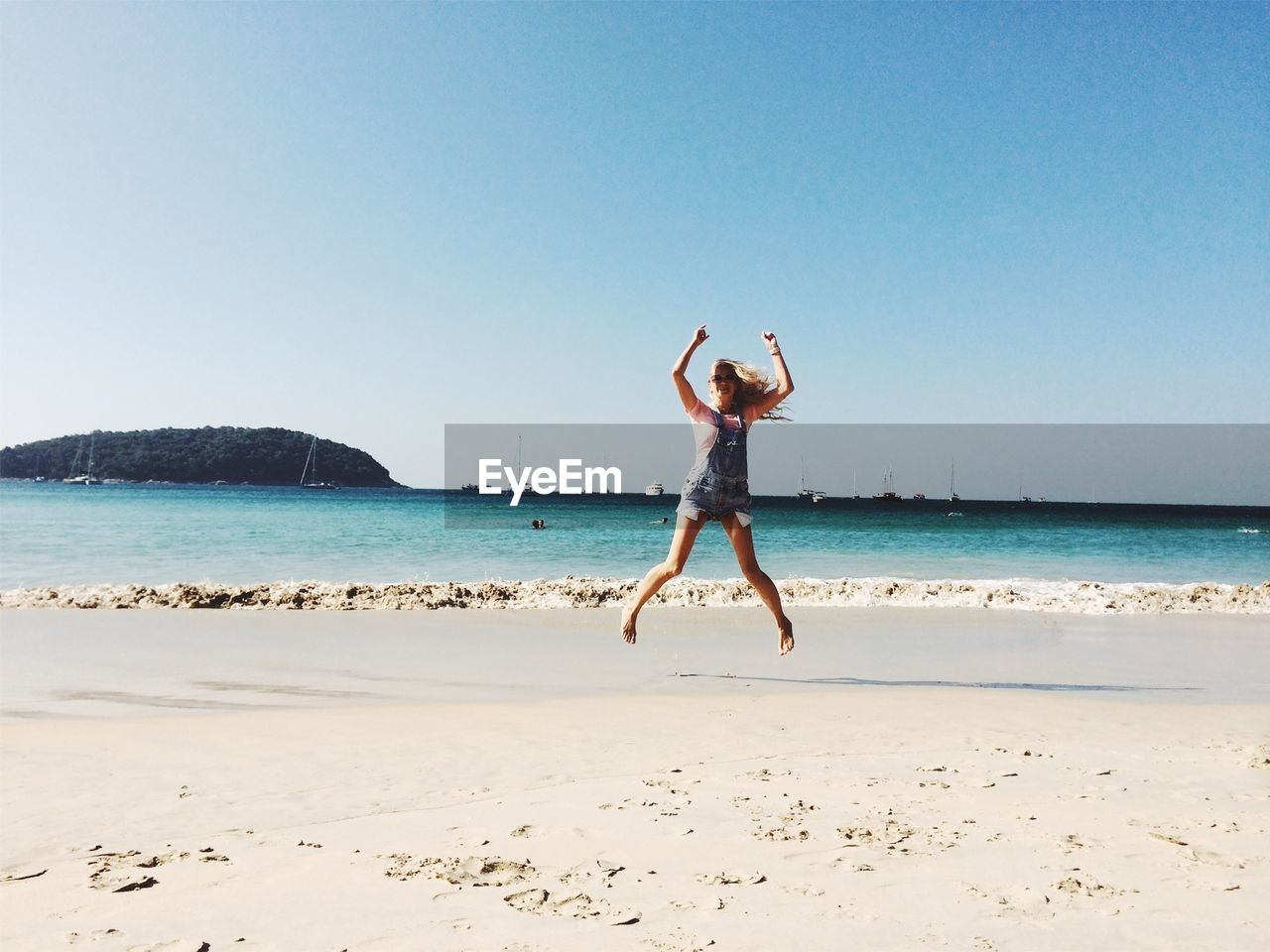 Full length of woman jumping at beach against clear sky