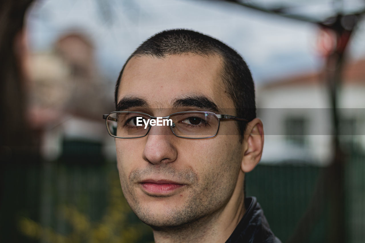 Close-up portrait of young man wearing eyeglasses while standing outdoors