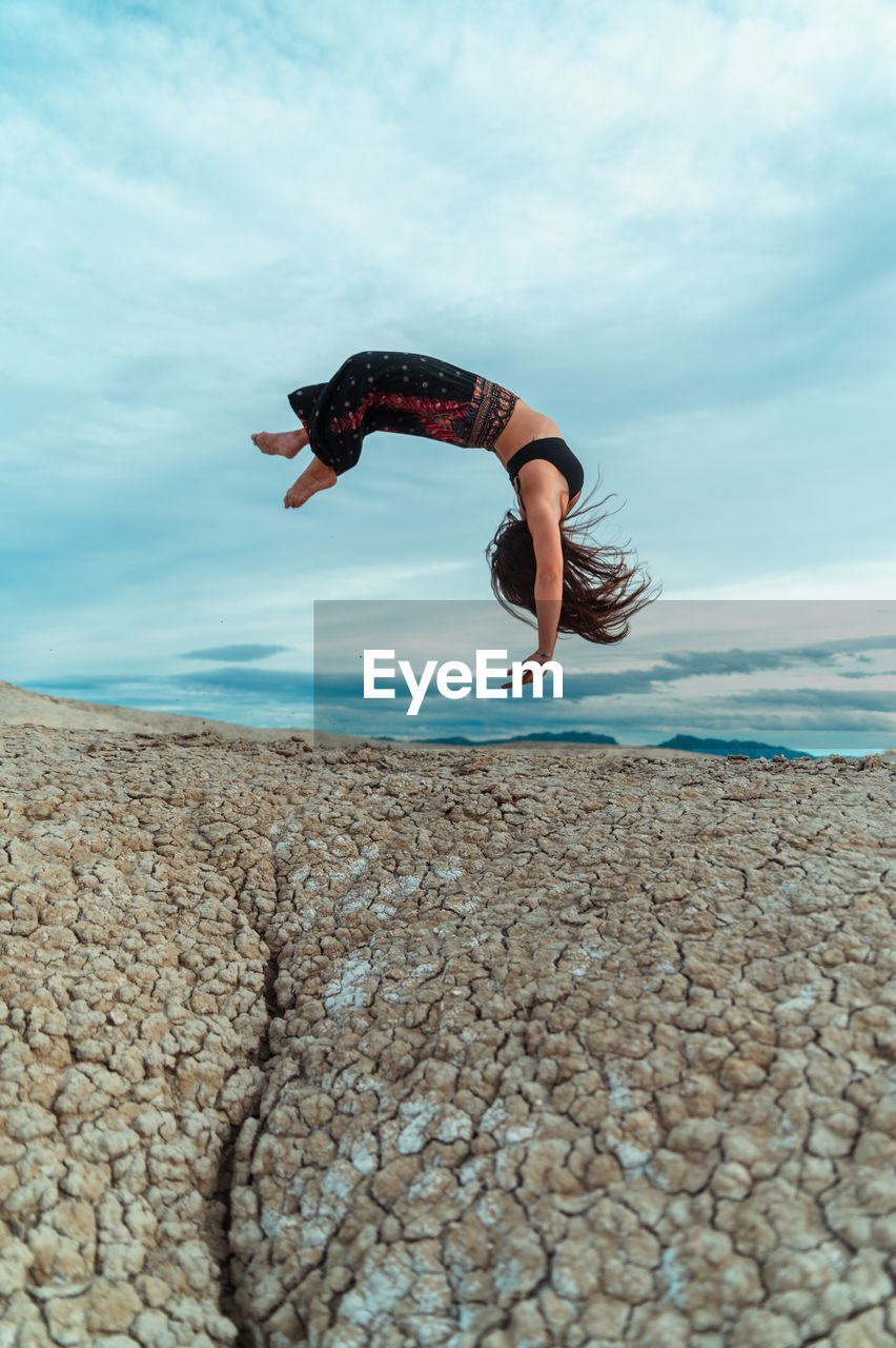 Full body of barefoot female balancing on handstand while practicing yoga pose in dried soil terrain