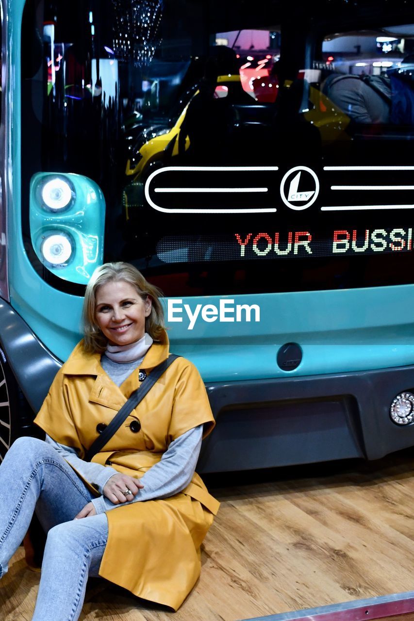 PORTRAIT OF A SMILING YOUNG WOMAN SITTING ON BUS