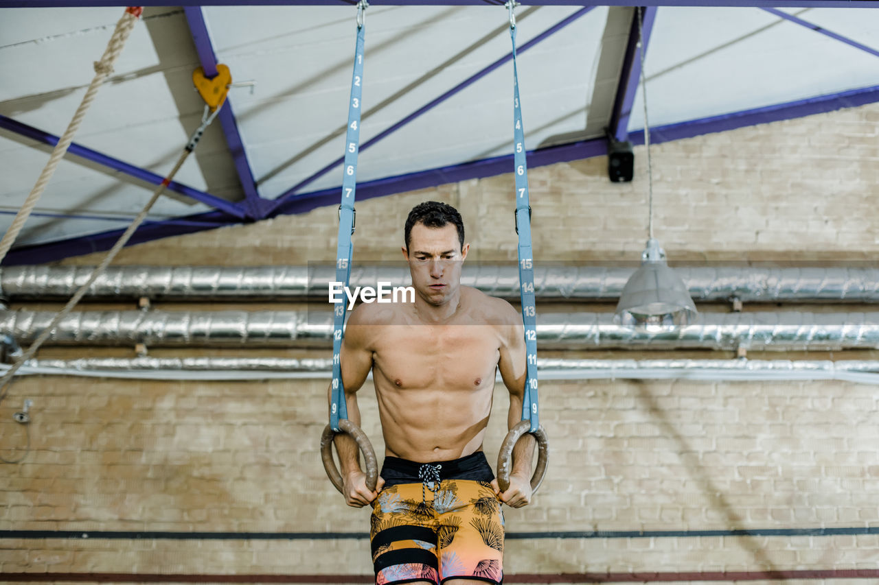 Male athlete with gymnastic rings doing exercise at gym