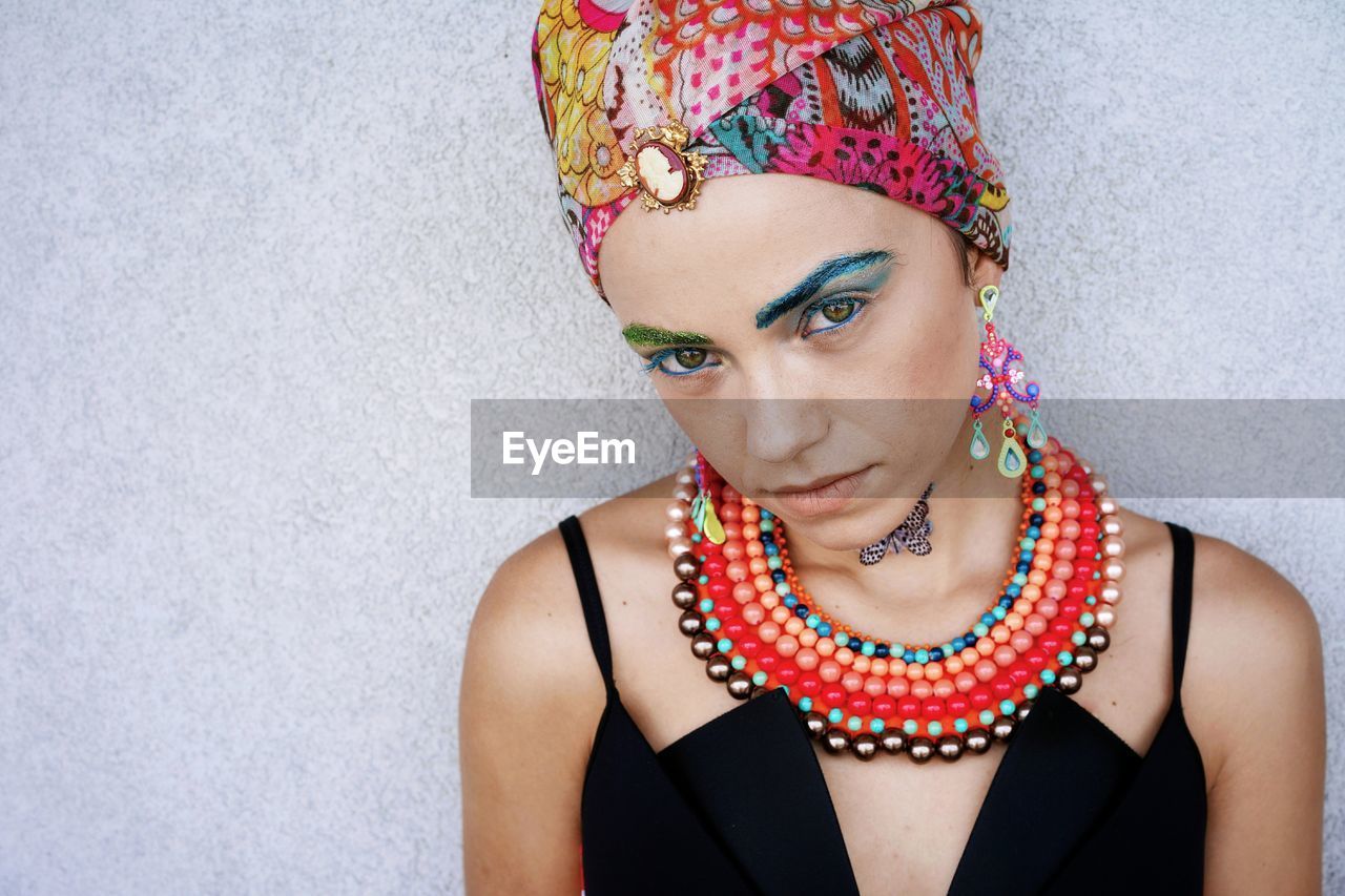 Portrait of confident young woman wearing headscarf and jewelries against wall