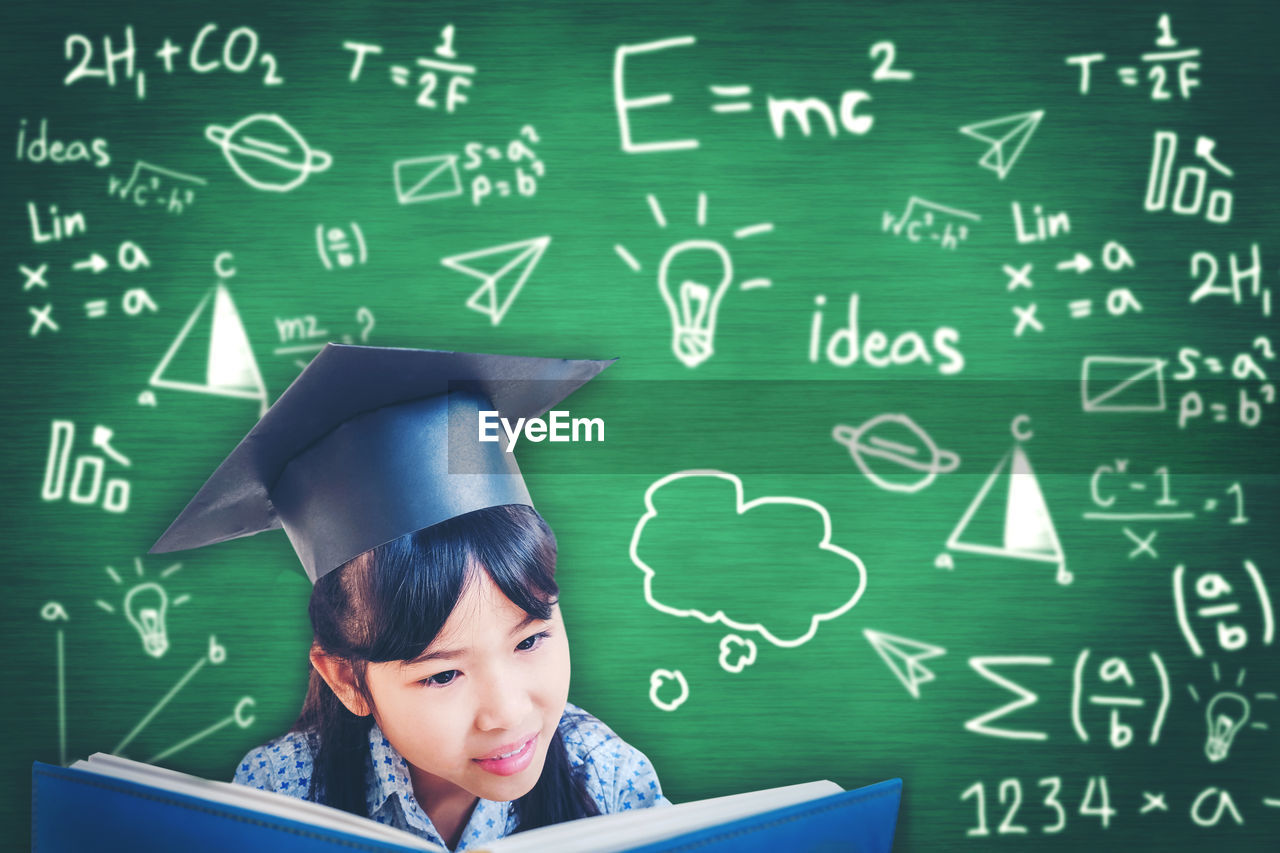 Teenage girl reading book against formulas on blackboard