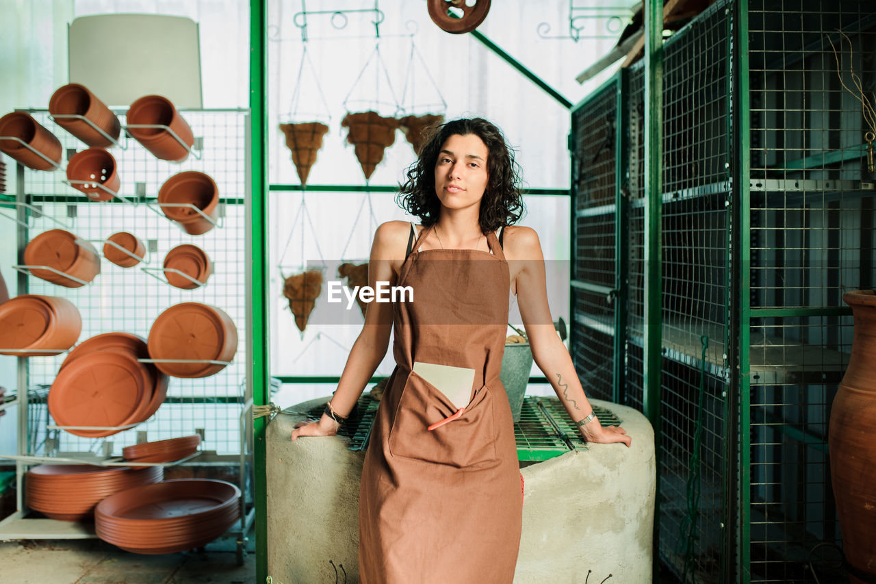 Portrait of smiling young woman standing against wall in workshop