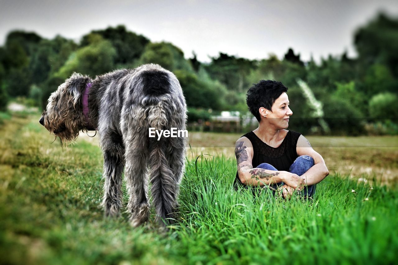 Smiling woman with irish wolfhound sitting on grassy field