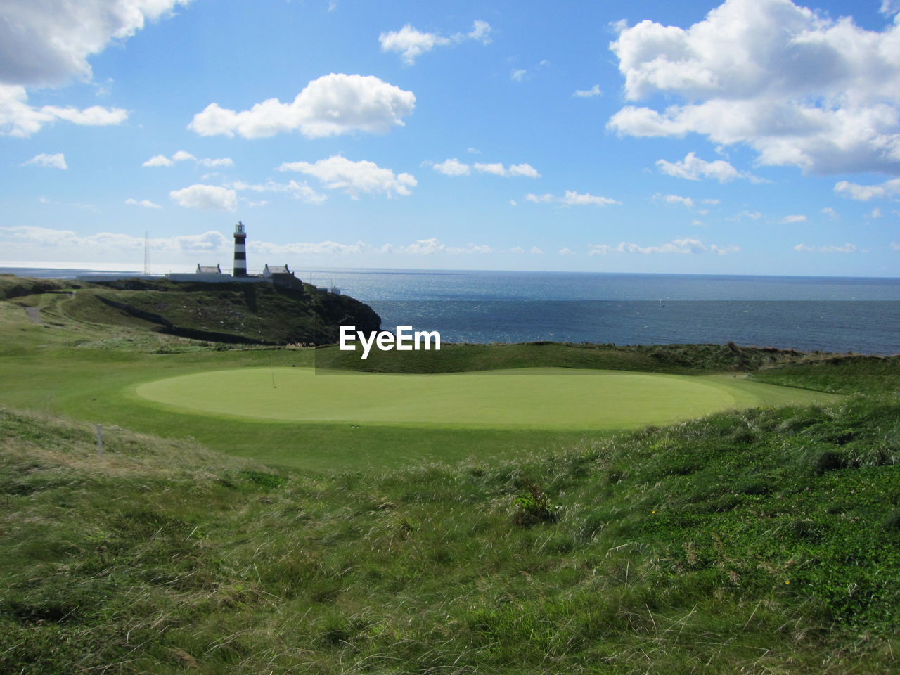 Golf course by sea against sky