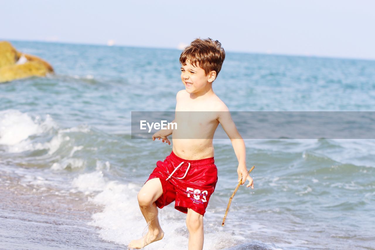 Full length of shirtless boy wading in sea