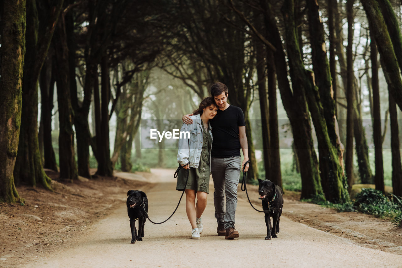 Couple embracing while walking dogs on a leash down a road in forest