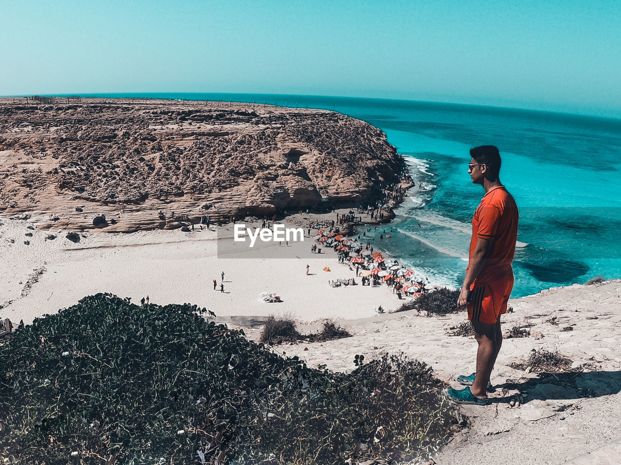 MEN STANDING ON ROCK AT BEACH AGAINST SKY