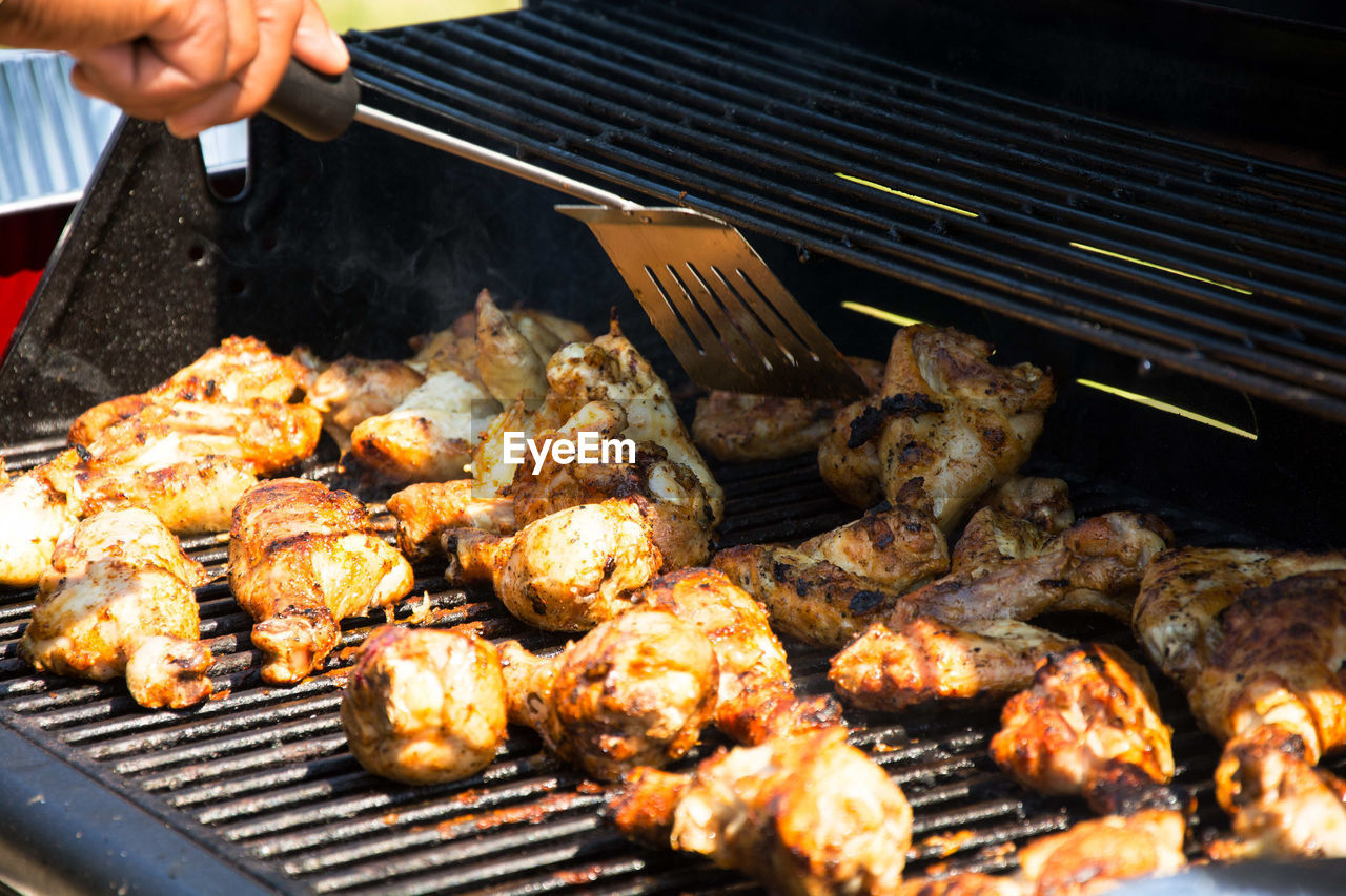 Cropped image of hand roasting chickens in barbecue