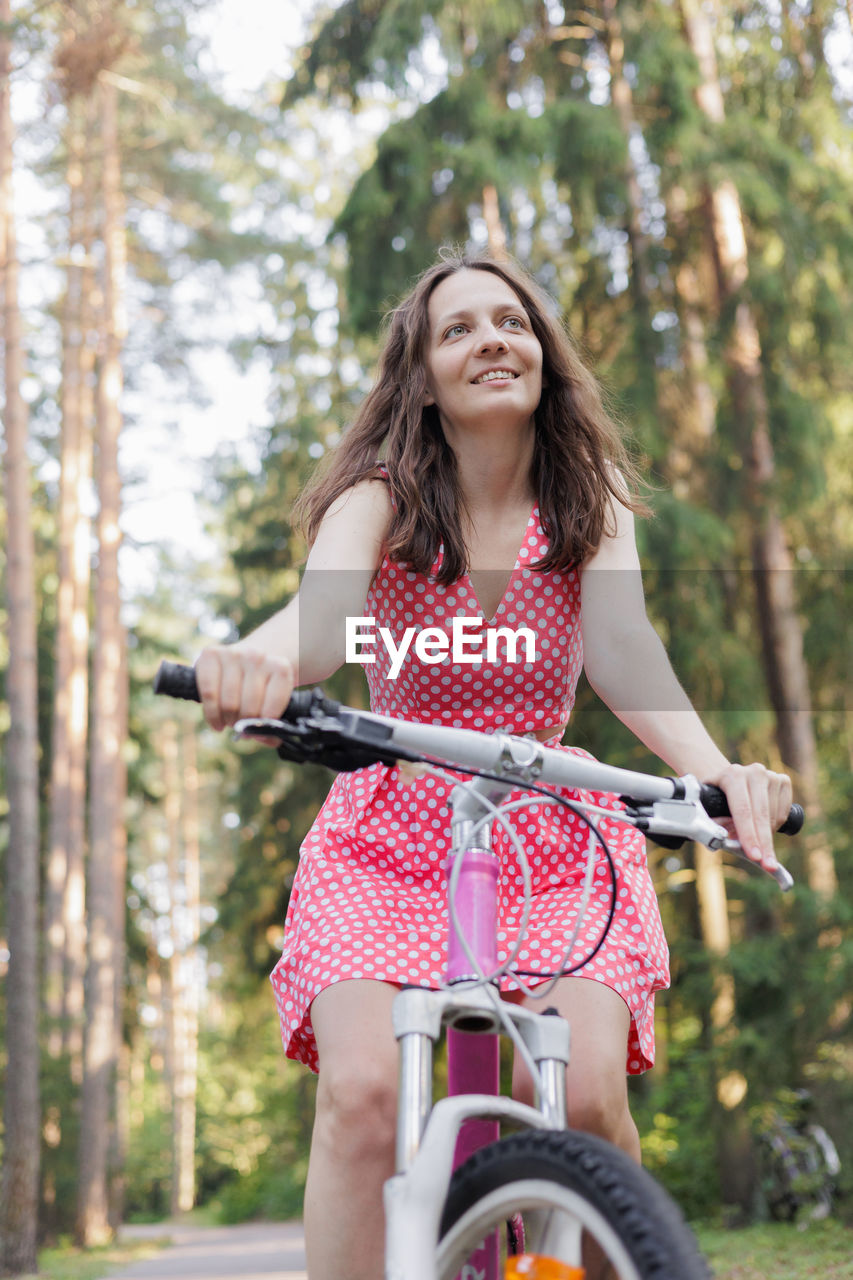 portrait of smiling young woman riding bicycle against trees