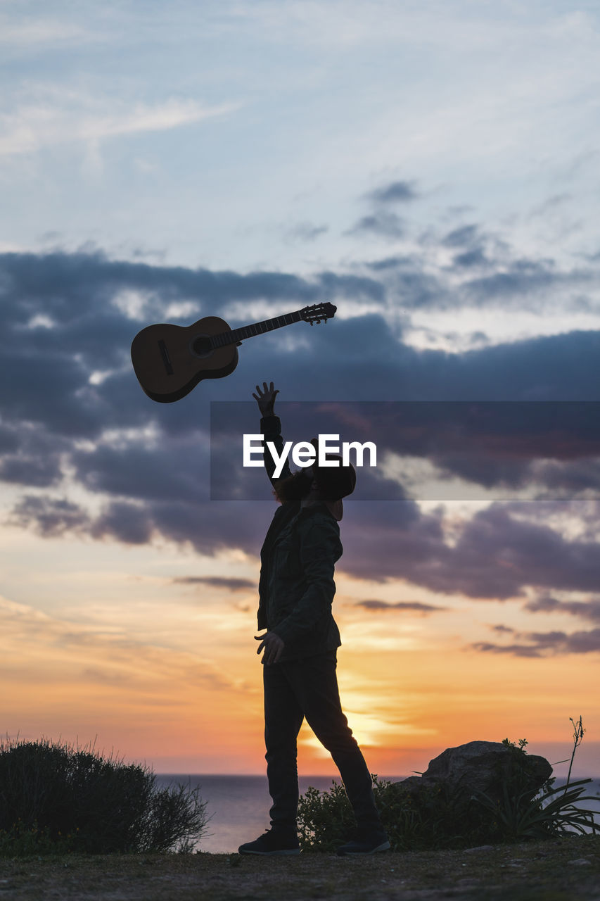 Man throwing guitar while standing on beach during sunset