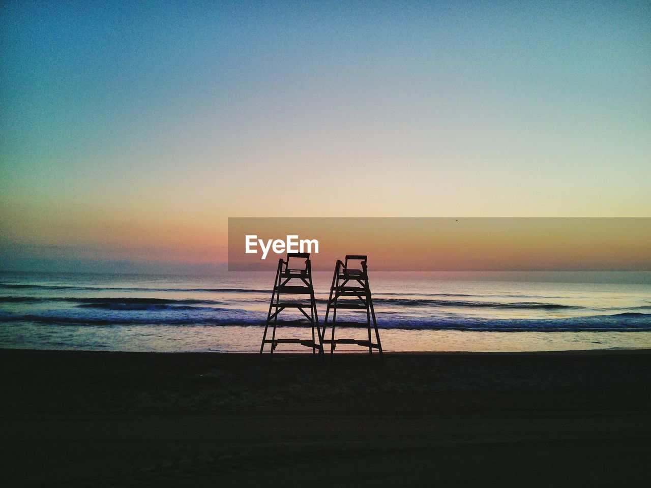 Lifeguard towers at beach against clear sky during sunset