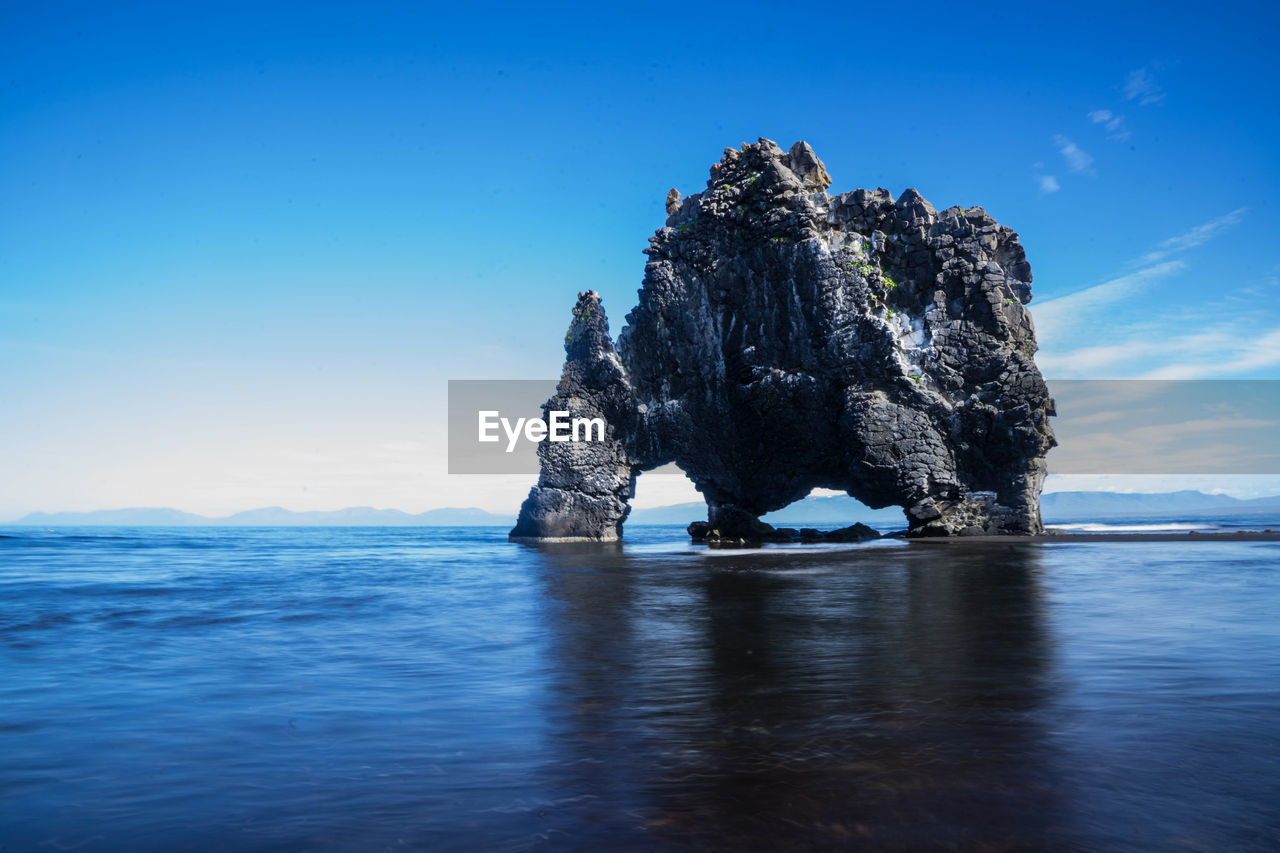 View of rock formation in sea against blue sky
