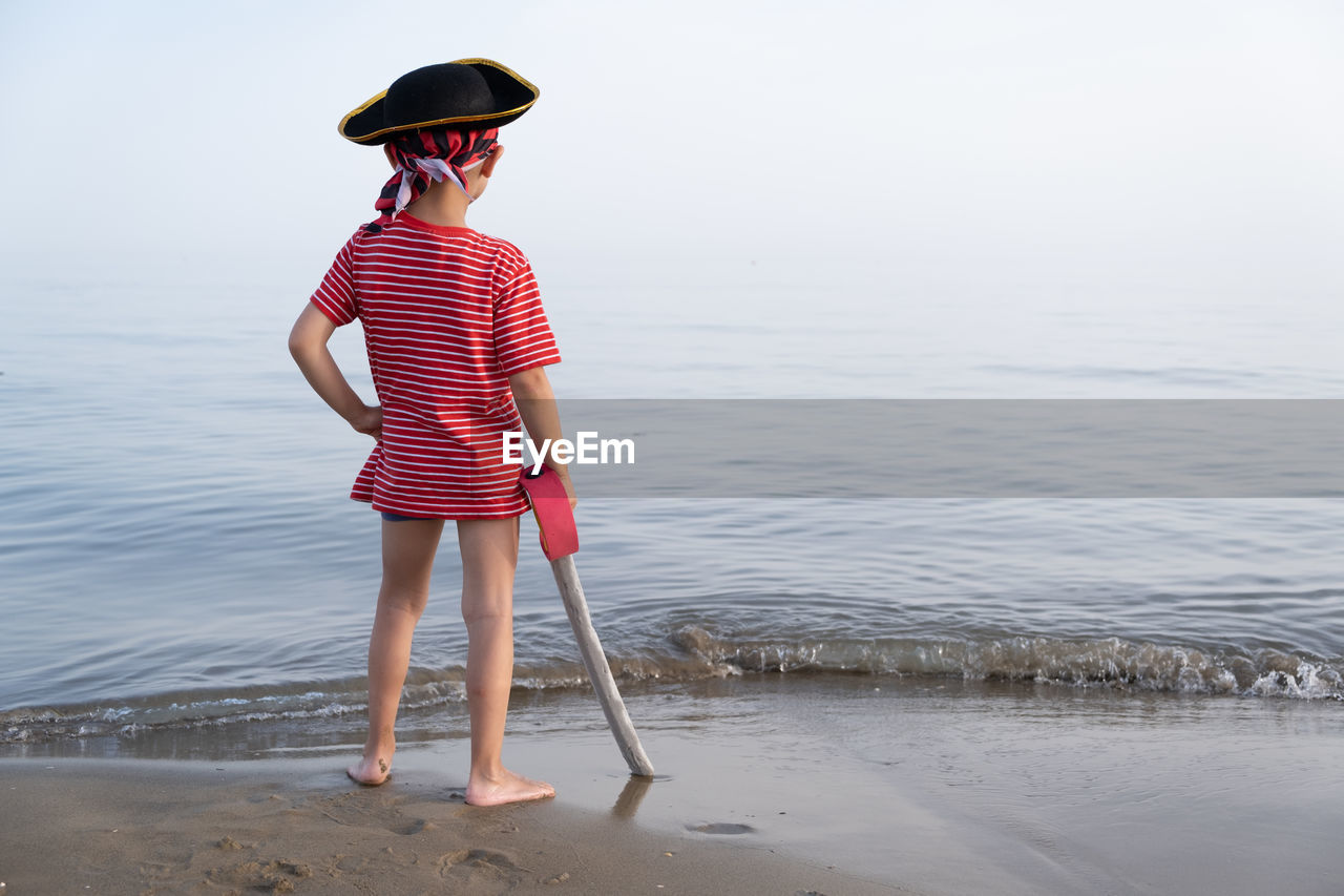 Rear view of boy wearing pirate costume standing in sea against sky