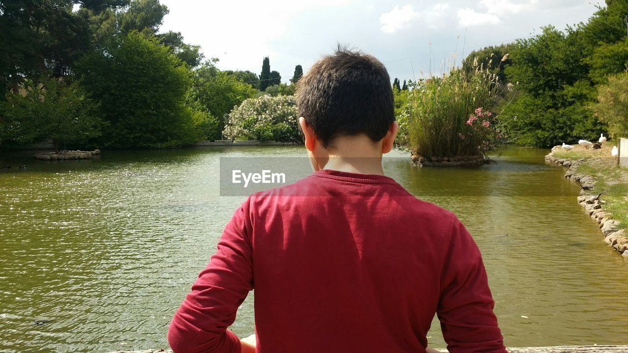 Rear view of boy standing in front of lake