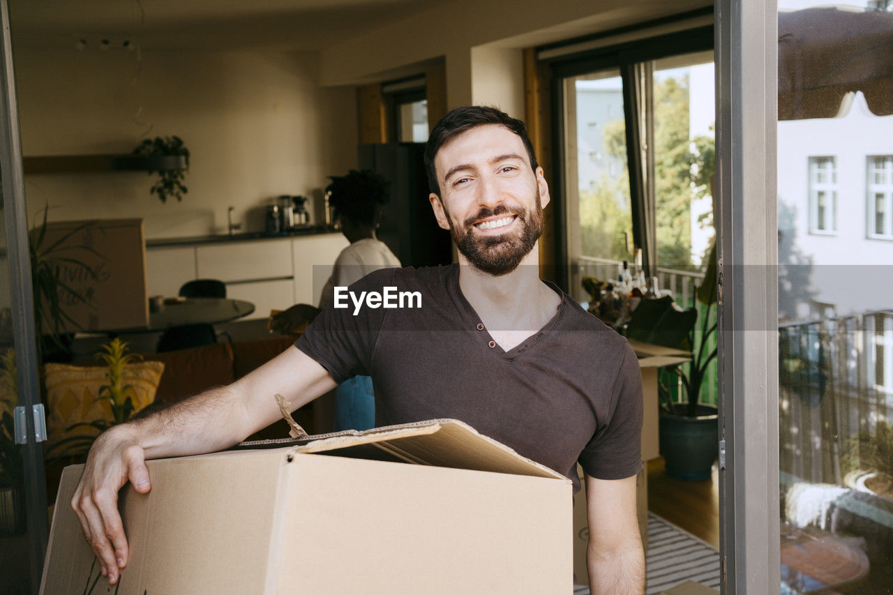 Portrait of smiling man carrying cardboard box at new home