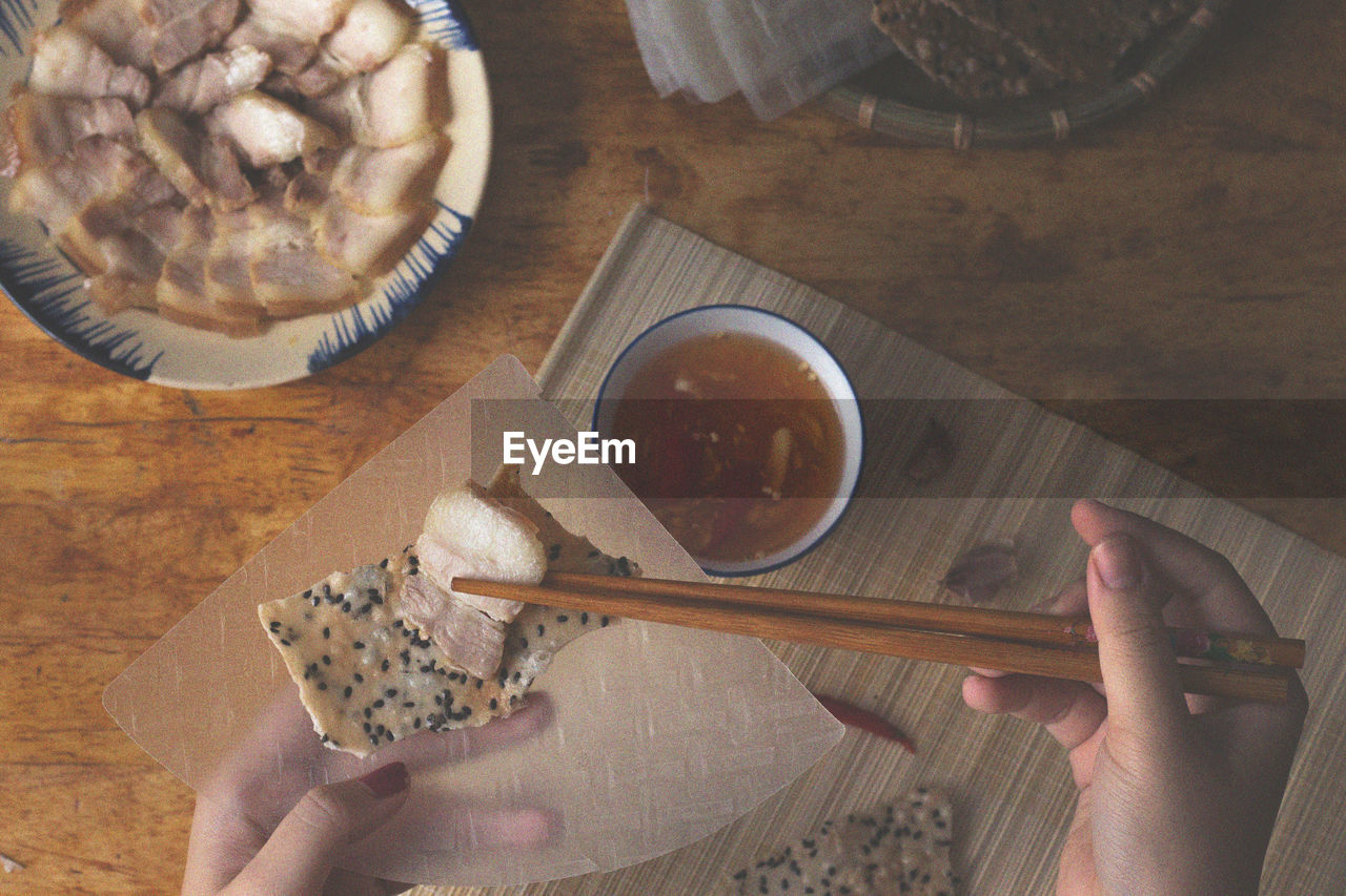 High angle view of hand holding meat with chopsticks over cracker