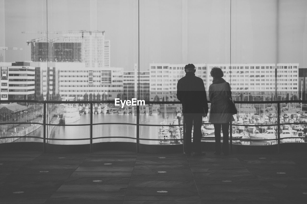 Rear view of man and woman standing against glass window in building