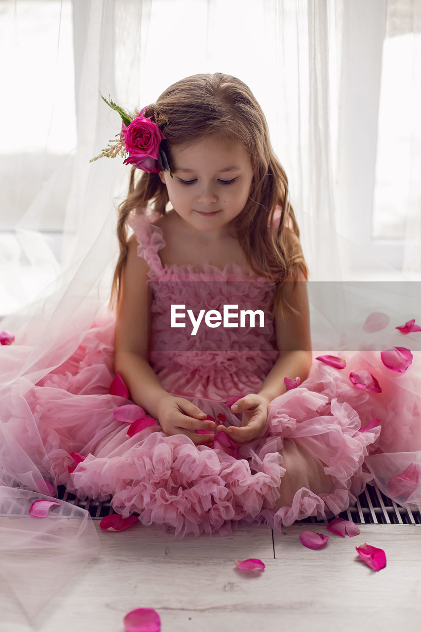 pink, child, childhood, women, one person, indoors, female, innocence, bedroom, dress, quinceañera, sitting, cute, domestic room, clothing, full length, bed, toddler, furniture, tutu, front view, baby, hairstyle, fashion, emotion, looking down, ruffle, flower, home interior, person, celebration, looking, smiling, brown hair, ballet tutu, long hair, happiness, lifestyles, flowering plant, event