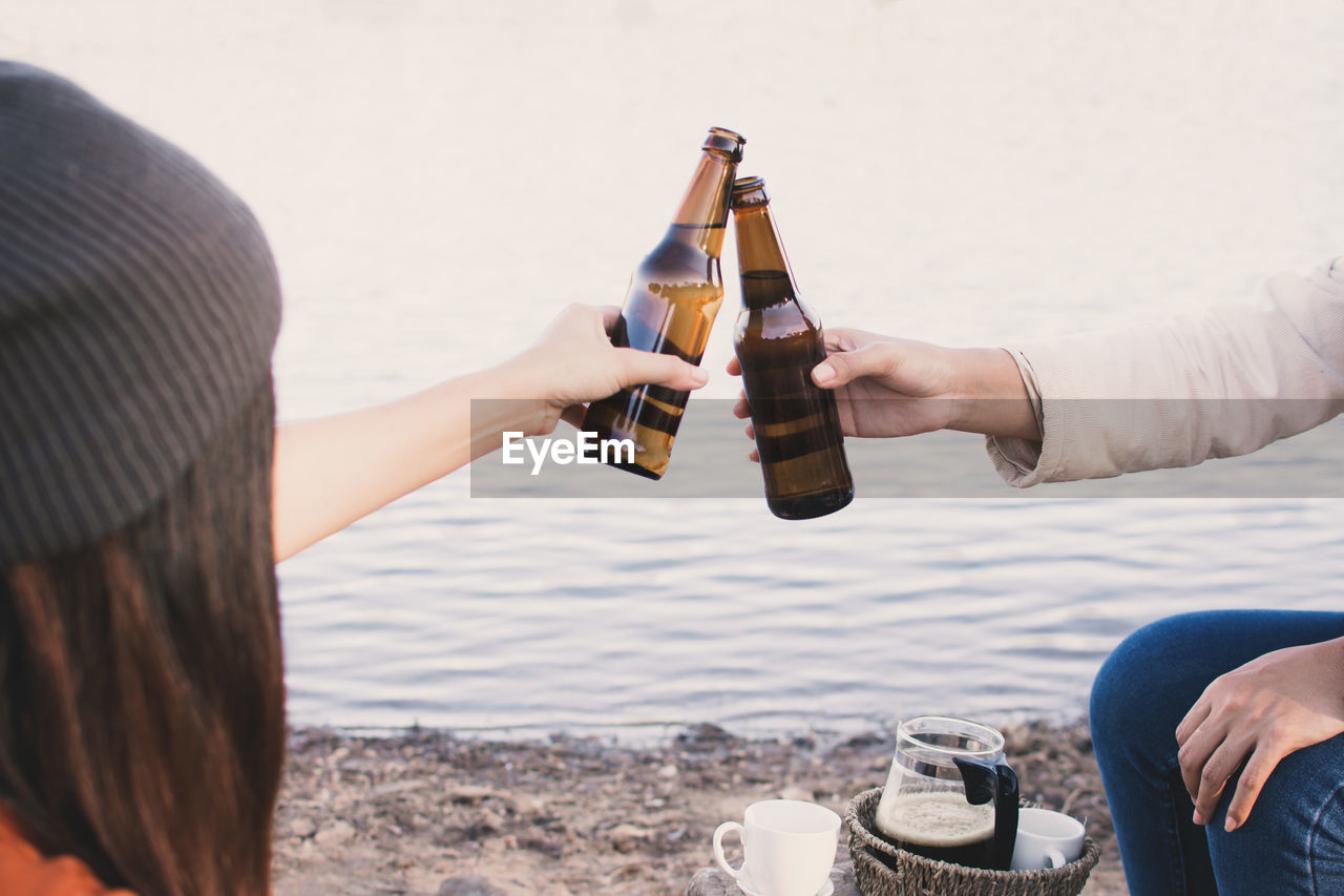 Friends toasting beer bottles at lakeshore
