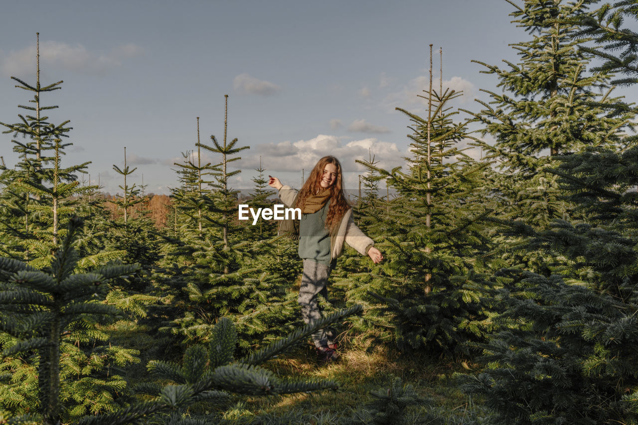 Happy girl with arms outstretched standing amidst fir tree farm