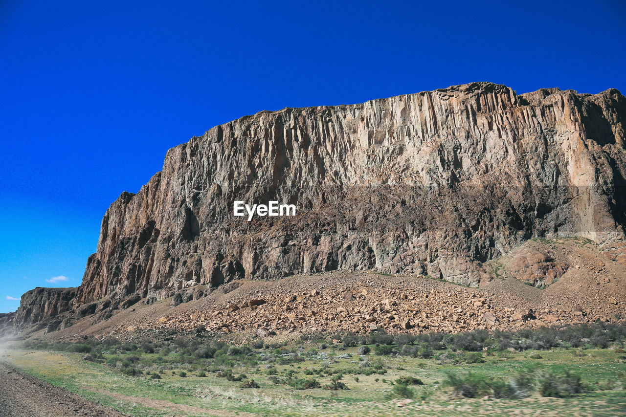 Low angle view of cliff against clear blue sky during sunny day