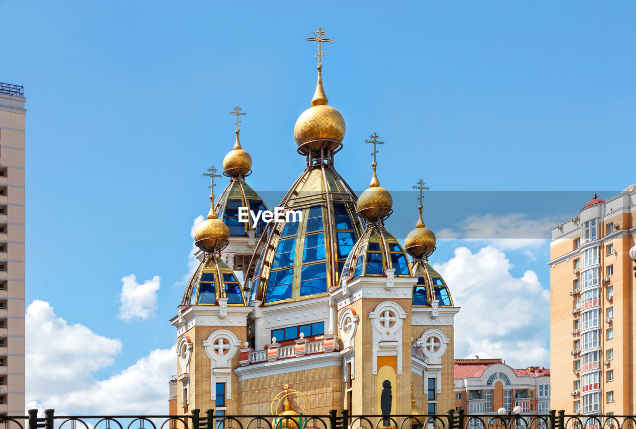 Golden domes of a christian church on glass roof facades among an urban residential area.