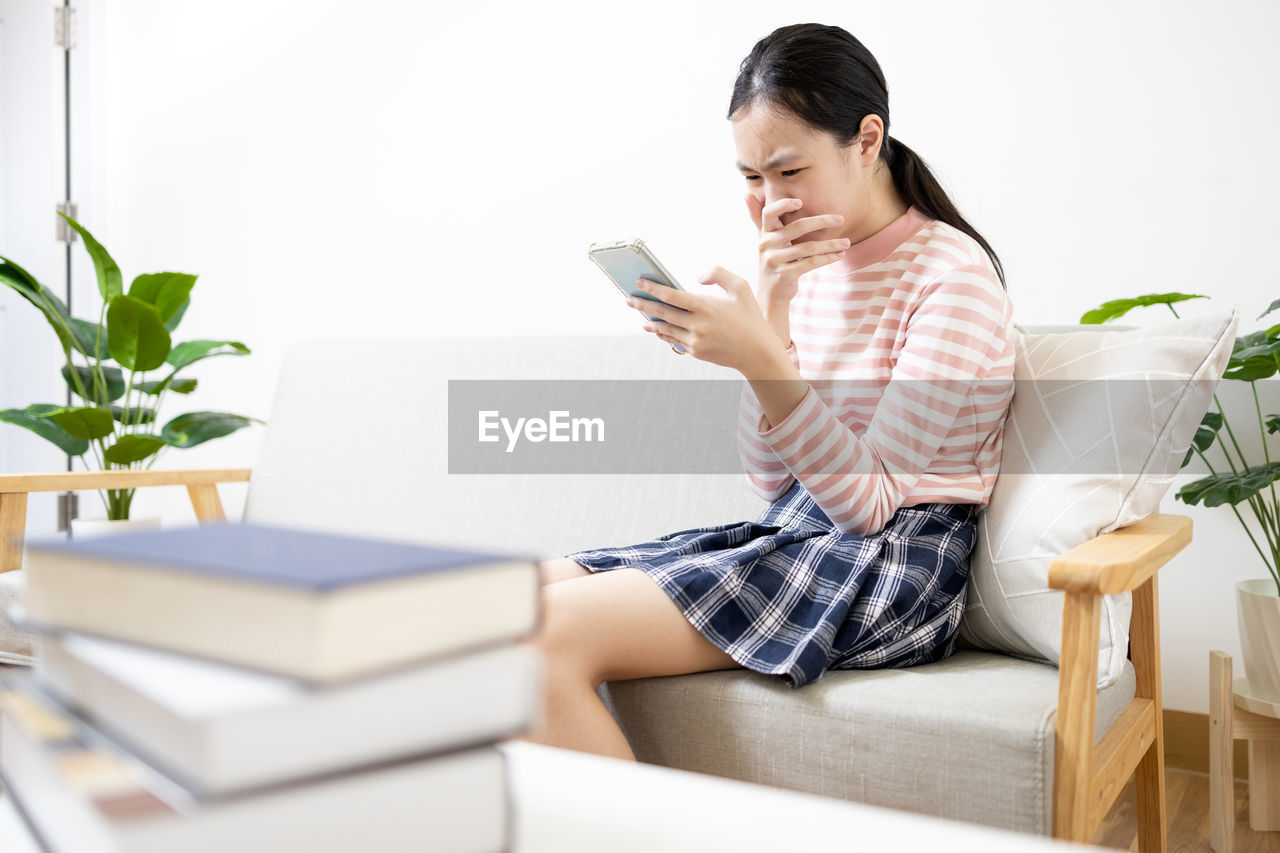 young woman using phone while sitting on sofa at home