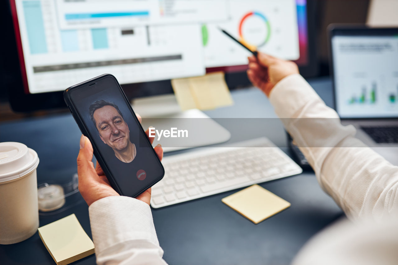 Woman entrepreneur having business video chat on smartphone with her business partner in office